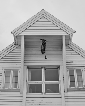 Black and white photograph of a white wooden house facade with symmetrical gable roof and central entrance.
