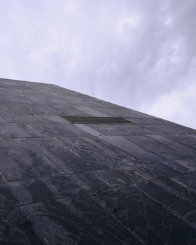 Dramatic diagonal composition of a dark, textured mountain slope against an overcast sky.