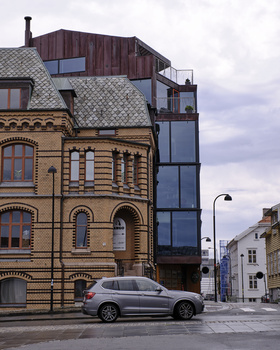 Contrasting architectural styles: ornate historic building adjacent to modern glass and metal structure with parked car in foreground.