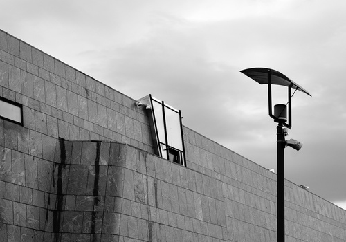 Modern street lamp silhouetted against concrete building facade and overcast sky.