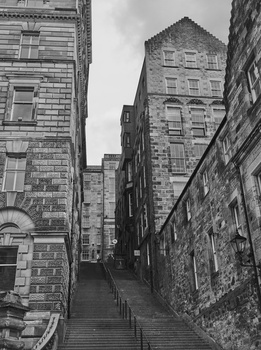 Narrow staircase descending between tall stone buildings in a historic urban alley.