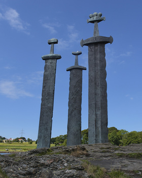 Three tall stone pillars with crosses on top stand against a blue sky in an open landscape.