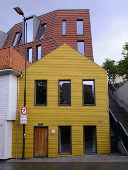 Bright yellow residential building with brown wooden door and black-framed windows against brick structures.