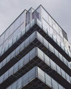 Modern concrete and glass corner building photographed from below against an overcast sky.
