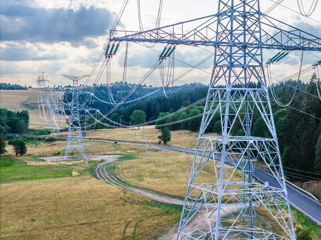High-voltage transmission tower spanning a rural landscape with power lines extending into the distance.