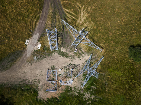Aerial view of electrical transmission tower substation surrounded by rural grassland and forest.