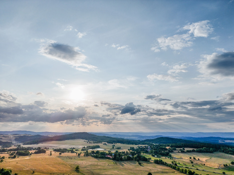 Rolling agricultural landscape beneath a dramatic cloudy sky at golden hour.