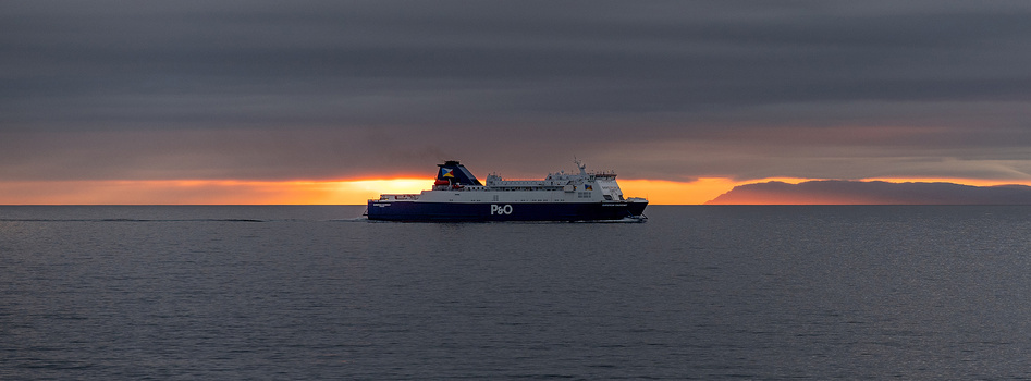 P&O ferry silhouetted against dramatic orange sunset over calm sea.