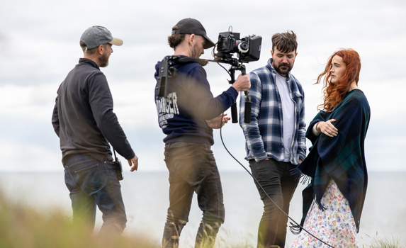 Film crew shooting outdoors with camera operator holding a cinema camera on stabilizer rig.