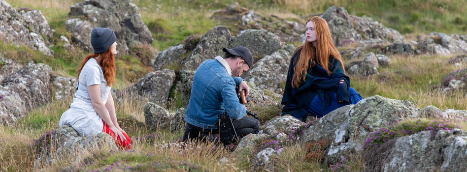 Three people with red hair sitting among moss-covered rocks in a natural outdoor setting.