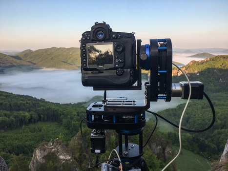 Professional camera mounted on tripod with motorized head overlooking misty lake and forested mountains at dawn.