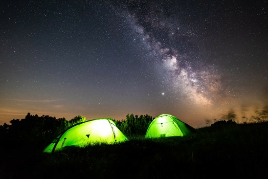 Two glowing green tents illuminated from within beneath the Milky Way galaxy at night.