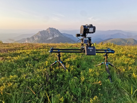 Camera slider rig with mounted cinema camera in a mountain meadow at golden hour.