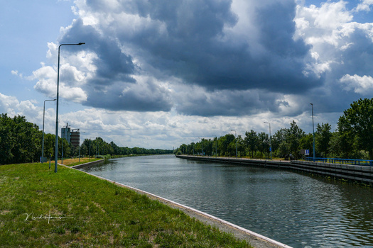 Wide canal lined with grass banks stretches toward the horizon under dramatic cloudy sky.