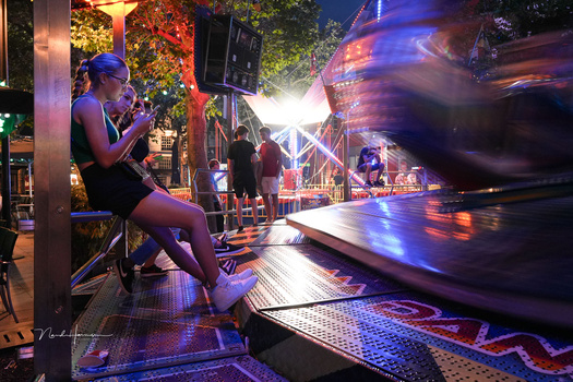 Woman sitting on a bench at night while a blurred bus passes by on a lit urban street.