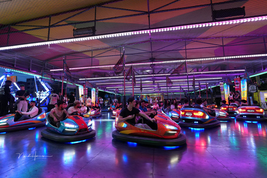 Bumper cars illuminated by vibrant neon lighting in an indoor arcade venue.