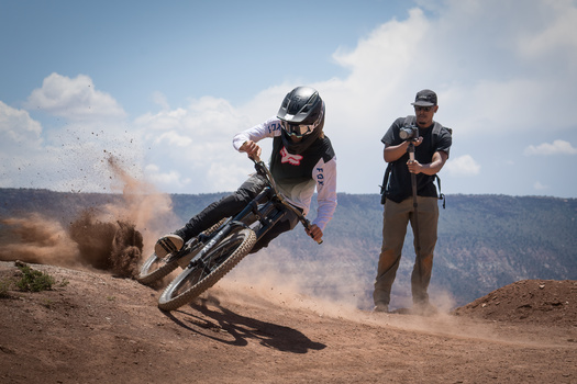 Downhill mountain bike rider leaning hard through a dusty turn on a dirt trail.