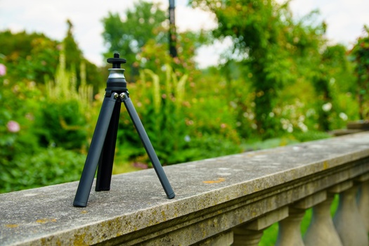Compact black tripod positioned on a concrete ledge overlooking a lush green landscape.