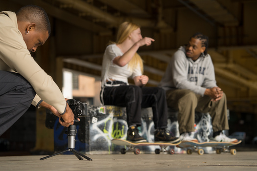 Photographer capturing a skateboarding scene with a camera while three young skateboarders wait nearby indoors.