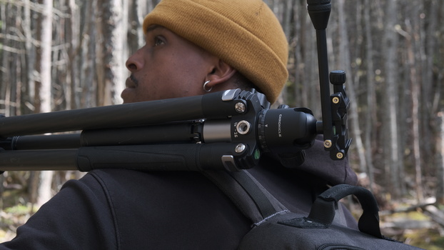 Filmmaker holding professional cinema camera rig with matte box and follow focus in wooded outdoor setting.
