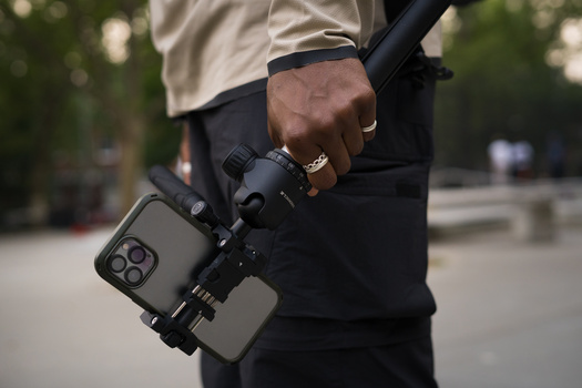 Videographer holding a professional camera rig with smartphone mounted on stabilizer.