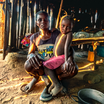 Woman crouching with child in sandy outdoor setting at dusk, warm golden light illuminating their figures.