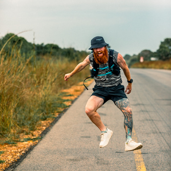 Runner with red beard and tattoo sprinting down a rural road lined with golden grass.