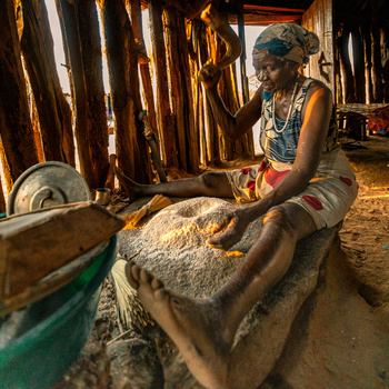 Woman working with grain or rice in a large wooden mortar, hands actively processing the ingredient.