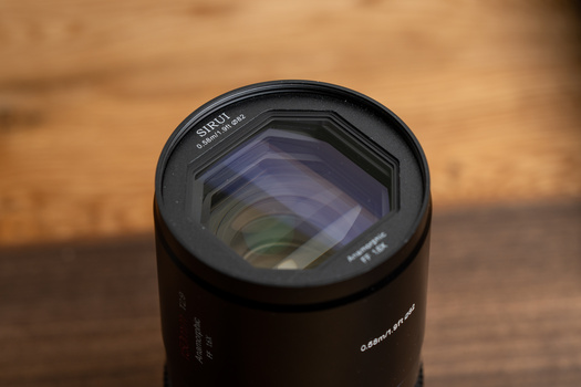 Telephoto zoom lens mounted on wooden surface with blurred warm background.