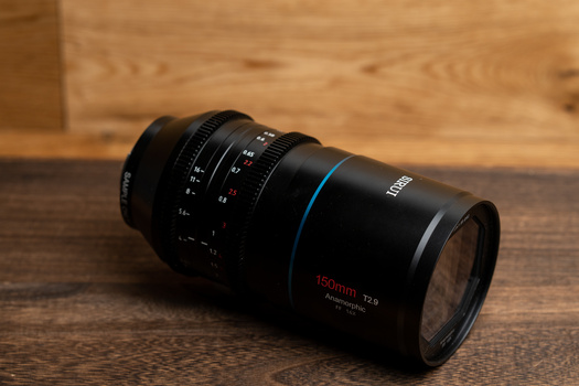 Black telephoto lens with blue accent ring resting on wooden surface.