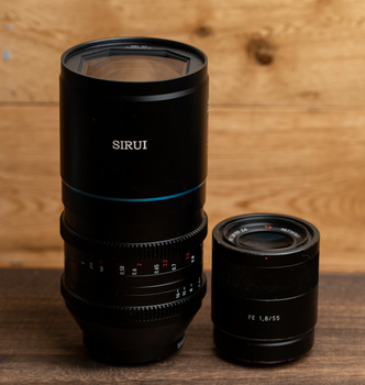 Two black camera lenses arranged on a wooden surface, with the larger SIRUI lens on the left and a smaller lens on the right.