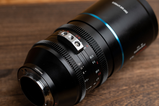 Telephoto cinema lens with focus ring and depth of field markings, photographed on wooden surface.