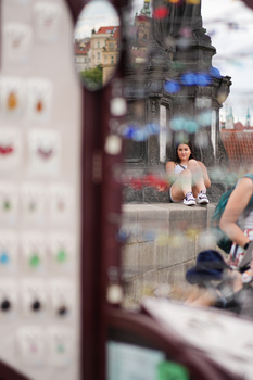 Woman seated at desk visible through window glass with reflections and out-of-focus foreground elements.