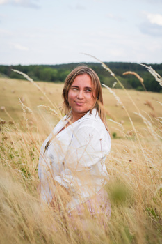 Woman in white shirt standing in golden wheat field, looking over shoulder toward camera.