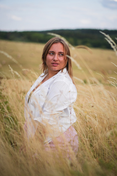 Woman in white shirt standing in golden wheat field, looking over shoulder at camera.