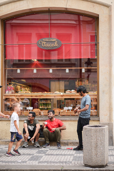 Four people seated on a bench outside a storefront with a bright pink facade and neon signage.