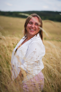 Woman in white shirt smiling at camera in golden grain field during daytime.