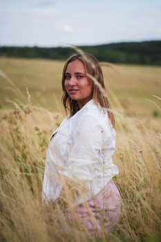 Woman in white shirt standing in golden wheat field, looking back toward camera.