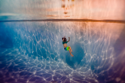 Snorkeler swimming underwater with rippling light patterns and sandy bottom visible above.