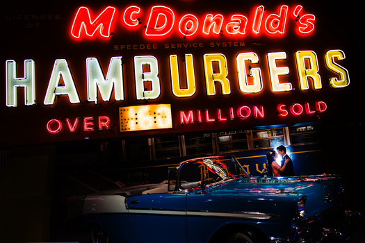 Vintage McDonald's neon sign displaying "Hamburgers" and "Over 1 Million Sold" above a parked blue classic car.