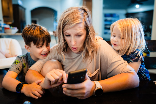 Woman and two children looking at a smartphone together indoors.