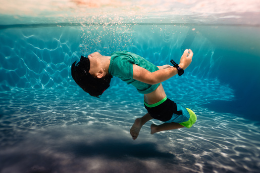 Male freediver in green shirt performing inverted pose underwater with bubbles rising toward surface.