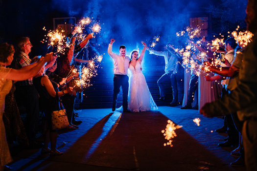 Newlyweds celebrate under a tunnel of sparklers held by wedding guests at night.