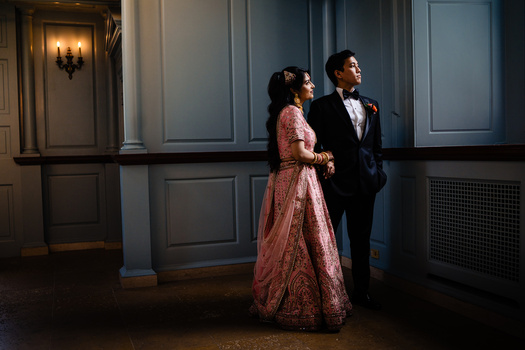 Couple in formal attire standing together in an elegantly paneled interior space with warm accent lighting.