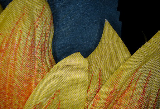 Close-up detail of layered yellow and orange fabric with red embroidered linear patterns against dark blue textile.
