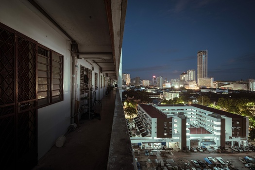 Covered walkway with wooden doors overlooking a sprawling cityscape at dusk.