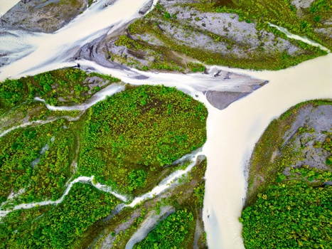 Aerial view of braided glacial rivers winding through dense green forest and rocky terrain.