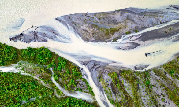 Aerial view of glacial rivers carving white channels through green tundra and gray terrain.