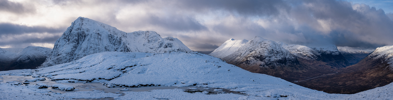 Snow-covered mountains and moorland under dramatic cloudy sky at dawn or dusk.