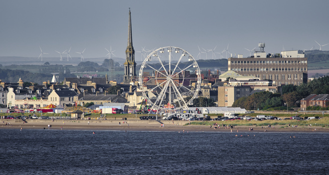 Large ferris wheel on a beach promenade with Victorian architecture and church spire in background.
